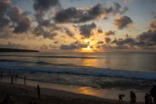 Illustration: Silhouetted people stand on a sandy beach during a cloudy sunset over the ocean.