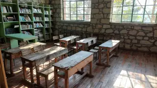 Illustration: An empty classroom with wooden desks and bookshelves under sunlight.