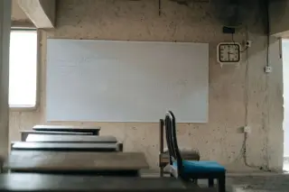 Illustration: An empty classroom with wooden desks, a chair, and a whiteboard.