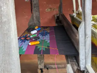 Illustration: Colorful spools of thread and scissors lie on a geometric woven fabric on a wooden loom.