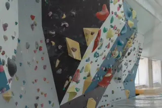 Illustration: An indoor climbing wall fitted with various colorful holds and geometric volumes.