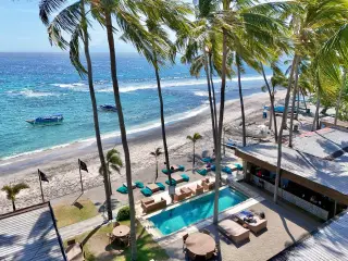 Illustration: Aerial view of a beachfront resort with palm trees, a swimming pool, and the ocean.