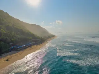 Illustration: An aerial view of a tropical sandy beach beside cliffs and ocean waves under sunlight.