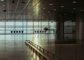 Illustration: An empty airport terminal hallway with large glass windows and rows of seats.