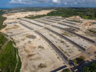 Illustration: An aerial view of a massive terraced land clearing and construction site on a coastal cliff.