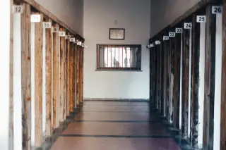 Illustration: An empty corridor lined with numbered wooden posts leading to a barred window.