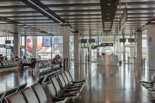 Illustration: An airport terminal waiting area with rows of seats and a view of an airplane outside.