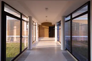 Illustration: An empty, modern hallway with floor-to-ceiling windows and sunlight casting shadows on the floor.
