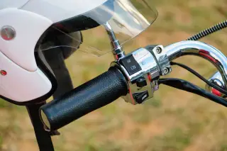 Illustration: A close-up shot of a motorcycle handlebar and a white helmet.