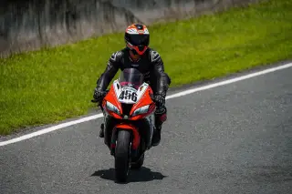 Illustration: A motorcycle racer in black gear rides a red sport bike on an asphalt track.