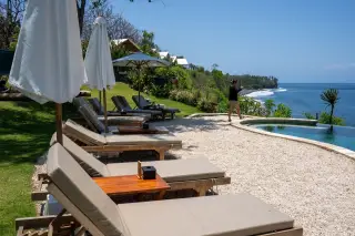 Illustration: Sun loungers and parasols by an infinity pool on a coastal cliff overlooking the sea.