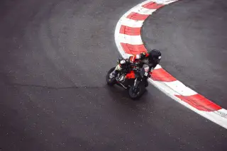 Illustration: A motorcycle racer leans into a sharp turn along a curved red-and-white race track kerb.