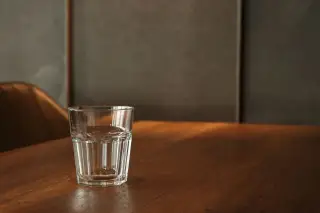 Illustration: A clear glass of water sits on a polished wooden table in warm lighting.