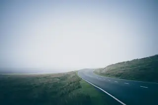 Illustration: An empty curving asphalt road winding through misty grassy hills.