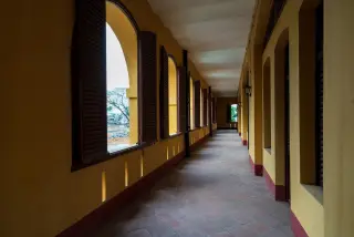 Illustration: An empty long corridor of an old yellow building with arched windows.