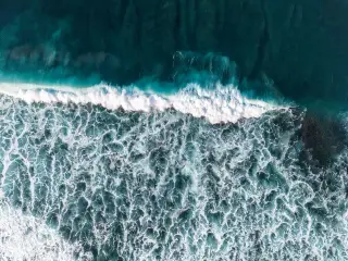 Illustration: An aerial view of turquoise ocean waves breaking into white seafoam.