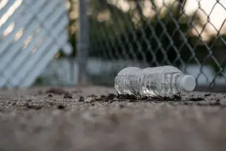 Illustration: A discarded plastic water bottle lying on the ground next to a chain-link fence.