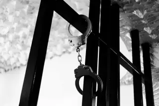 Illustration: A pair of metal handcuffs hanging from black metal bars in black and white.