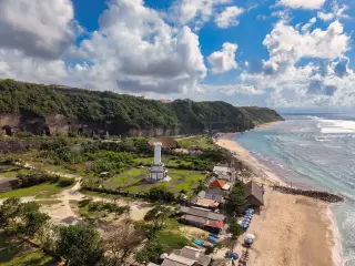Illustration: An aerial view of a coastal area with a white tower, beach, and green cliffs.