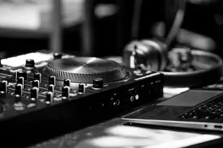 Illustration: A monochrome close-up of a DJ controller, headphones, and laptop on a desk.