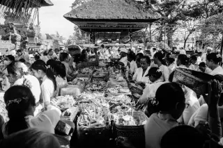 Illustration: Black and white shot of Balinese devotees gathered with offerings at a temple courtyard.