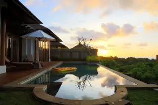 Illustration: A swimming pool and patio loungers at a tropical resort during sunset.