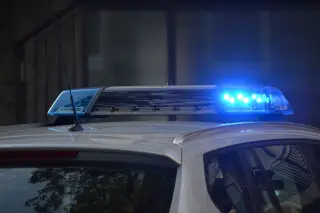 Illustration: Close-up of a police car light bar flashing blue lights on the vehicle roof.