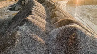 Illustration: Large mounds of gravel and sand in a quarry under sunlight.