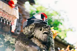 Illustration: A stone statue wearing a checkered cloth headpiece at a Balinese temple.