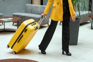 Illustration: A woman in a yellow jacket pulling a bright yellow suitcase in a spacious lobby.