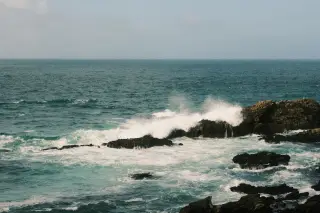 Illustration: Ocean waves crashing against dark coastal rocks under a clear sky.