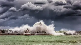 Illustration: Large ocean waves crash over a stone pier and boat under dramatic stormy skies.
