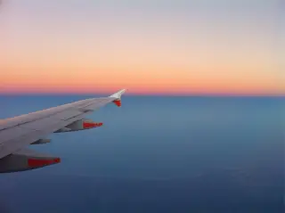 Illustration: An airplane wing flying above the horizon during sunset or sunrise.