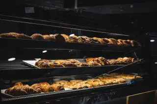 Illustration: Pastries and freshly baked bread arranged on display shelves inside a bakery counter.