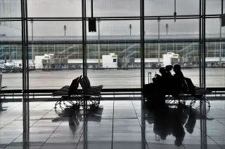 Illustration: Silhouettes of passengers sitting on chairs at an airport gate overlooking the tarmac.