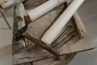 Illustration: A hammer, chisels, and paper rolls resting on a weathered wooden stool.