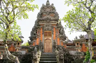 Illustration: An ornate stone Balinese temple gate framed by trees under daylight.