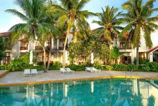Illustration: A swimming pool and sun loungers in front of a tropical resort villa surrounded by palm trees.