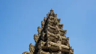 Illustration: The ornate stone spire of a traditional Balinese temple tower set against a clear blue sky.