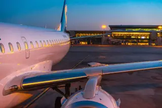 Illustration: A commercial airplane parked on the tarmac facing an illuminated airport terminal at dusk.