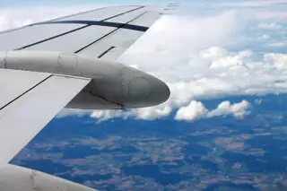 Illustration: An airplane wing seen from a window high above clouds and land below.