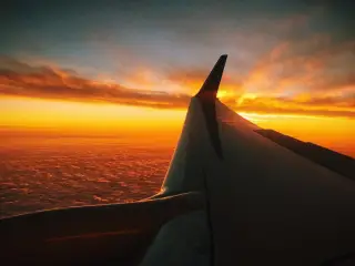 Illustration: An airplane wing flying high above clouds during a golden sunset.
