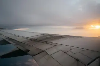 Illustration: View of an airplane wing flying above the clouds during sunset.