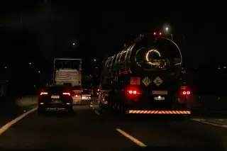 Illustration: A large tanker truck and other vehicles drive on a highway at night.