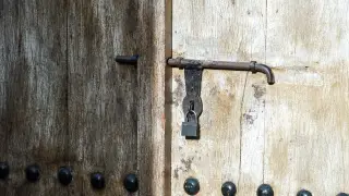 Illustration: A close-up of a locked weathered wooden door with an iron latch and padlock.