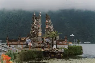 Illustration: A Balinese split gate temple structure beside a lake with forested hills and mist.