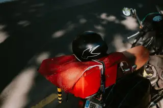 Illustration: A helmet rests on the back rack of a parked scooter on an asphalt street.