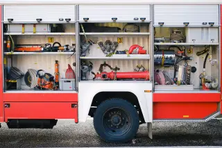 Illustration: Open side compartments of a fire truck loaded with rescue equipment and hoses.