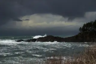 Illustration: Rough ocean waves crashing against dark rocky cliffs beneath a dark, overcast stormy sky.