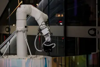 Illustration: A white robotic arm equipped with a camera mounted indoors against dark glass panels.